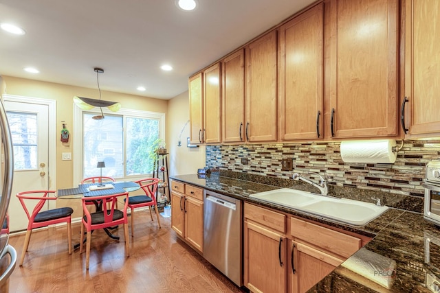 kitchen with light wood-type flooring, pendant lighting, a sink, stainless steel appliances, and decorative backsplash