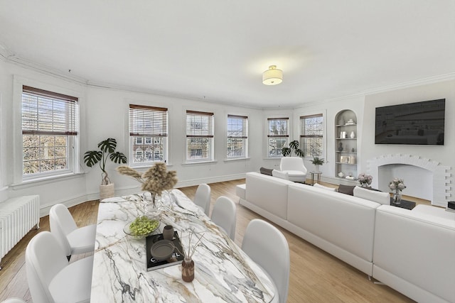 dining area with radiator heating unit, a brick fireplace, light wood-style flooring, and built in features