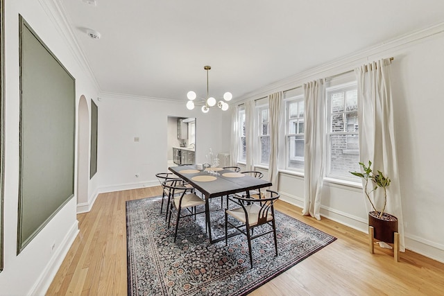 dining area with arched walkways, light wood-style flooring, a notable chandelier, baseboards, and ornamental molding