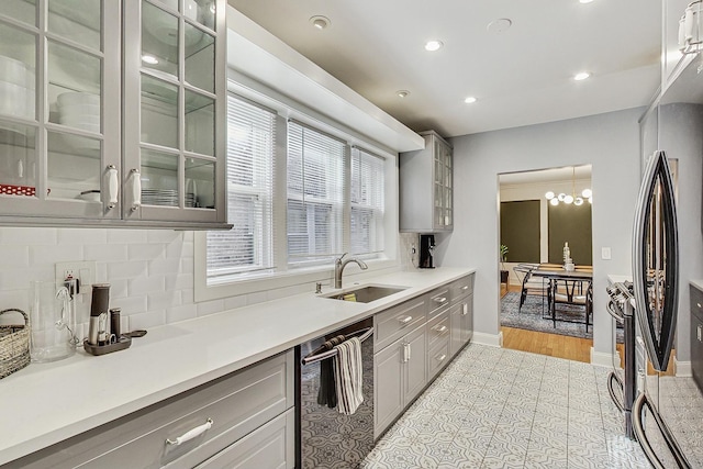 kitchen featuring decorative backsplash, dishwasher, gray cabinets, light countertops, and a sink