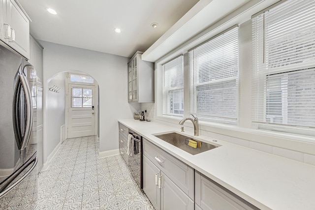 kitchen featuring arched walkways, recessed lighting, a sink, stainless steel fridge, and dishwasher