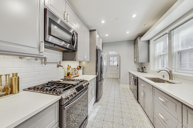 kitchen with appliances with stainless steel finishes, gray cabinets, a sink, and light countertops