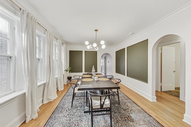 dining room featuring arched walkways, light wood-style flooring, baseboards, ornamental molding, and an inviting chandelier