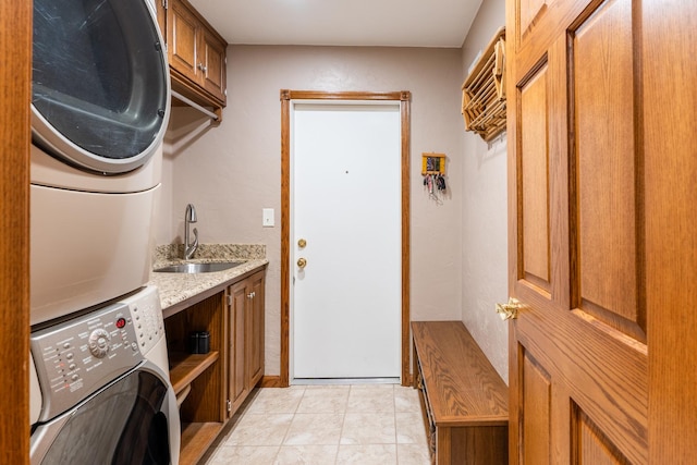 clothes washing area with stacked washer and dryer, light tile patterned floors, cabinet space, and a sink