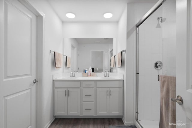 bathroom with a stall shower, double vanity, a sink, and wood finished floors