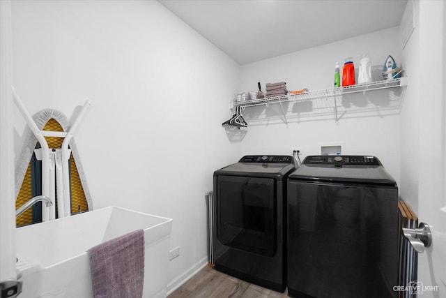 clothes washing area featuring baseboards, wood finished floors, washing machine and clothes dryer, and laundry area