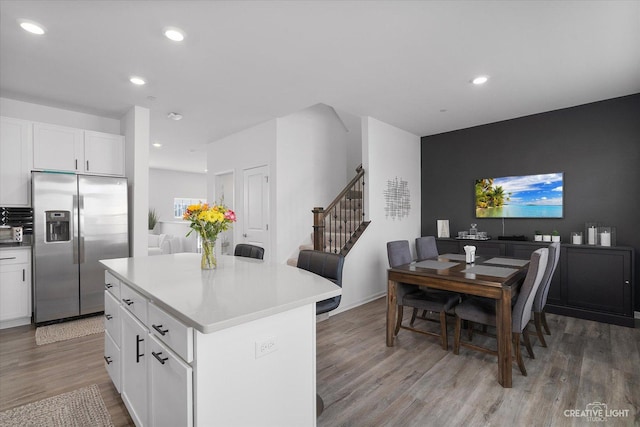 kitchen featuring light wood-style flooring, stainless steel fridge, light countertops, a kitchen island, and white cabinets