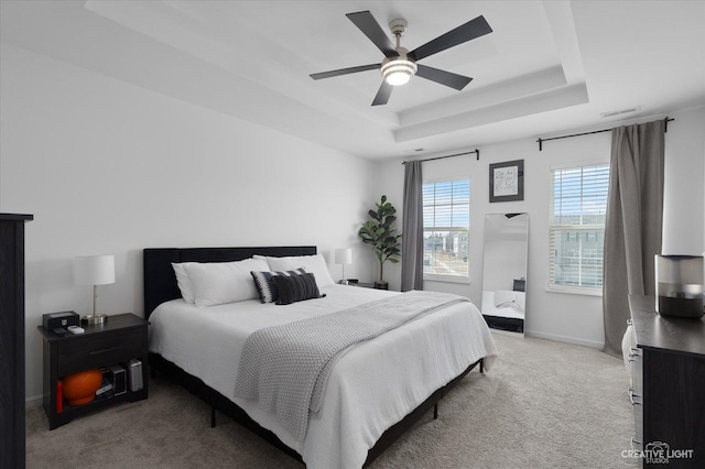 bedroom featuring visible vents, a tray ceiling, baseboards, light carpet, and a ceiling fan