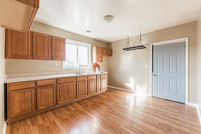 kitchen with light countertops, light wood-style flooring, brown cabinetry, and a sink