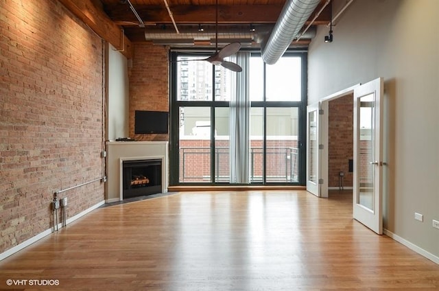 unfurnished living room with a high ceiling, a fireplace with flush hearth, wood finished floors, and brick wall