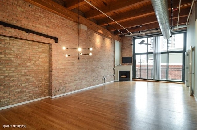 unfurnished living room with a fireplace, brick wall, a high ceiling, and wood finished floors