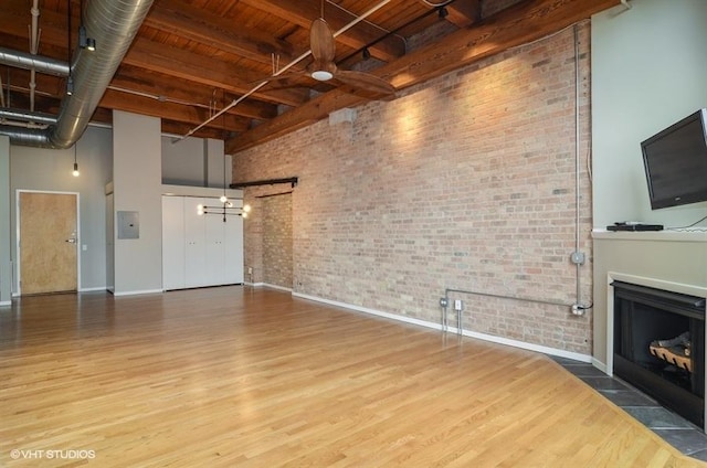 unfurnished living room with brick wall, a fireplace with flush hearth, wood finished floors, and a towering ceiling