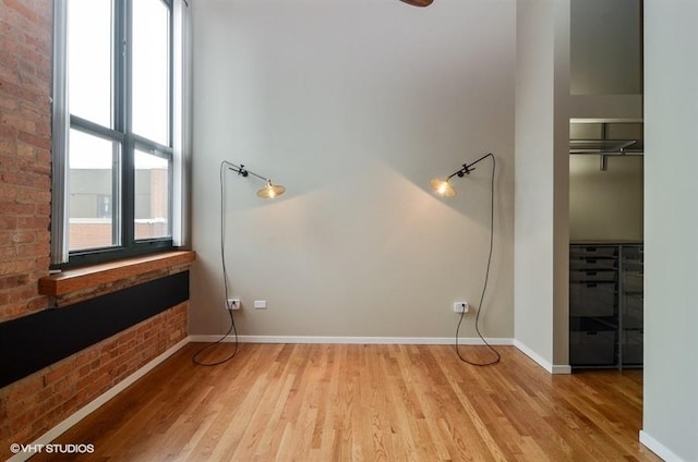 empty room with light wood finished floors, brick wall, and baseboards