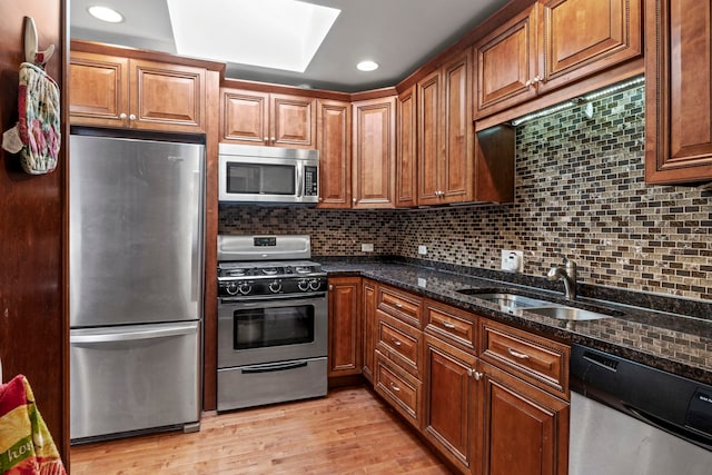 kitchen featuring light wood finished floors, decorative backsplash, dark stone counters, appliances with stainless steel finishes, and a sink