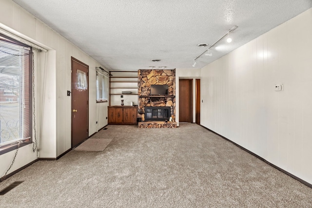 unfurnished living room with carpet floors, rail lighting, visible vents, a stone fireplace, and a textured ceiling