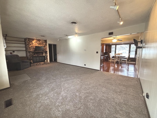 unfurnished living room with carpet floors, visible vents, a textured ceiling, and a stone fireplace