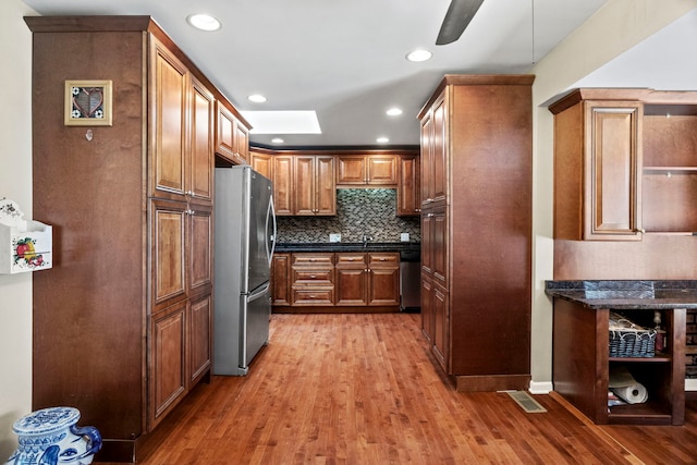 kitchen with stainless steel appliances, visible vents, decorative backsplash, light wood finished floors, and brown cabinetry