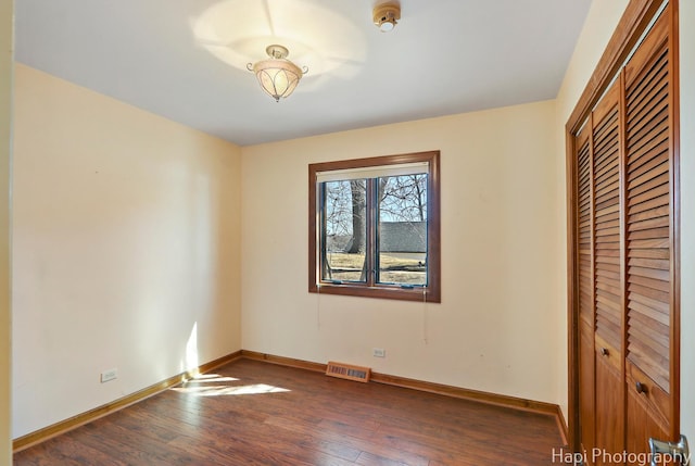 unfurnished bedroom featuring hardwood / wood-style floors, visible vents, baseboards, and a closet