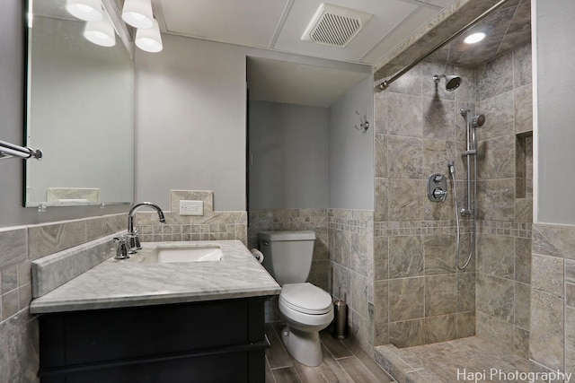 full bathroom with a tile shower, visible vents, toilet, and tile walls