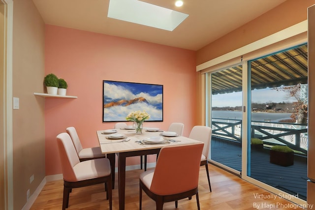 dining room with baseboards, a skylight, a water view, and light wood finished floors