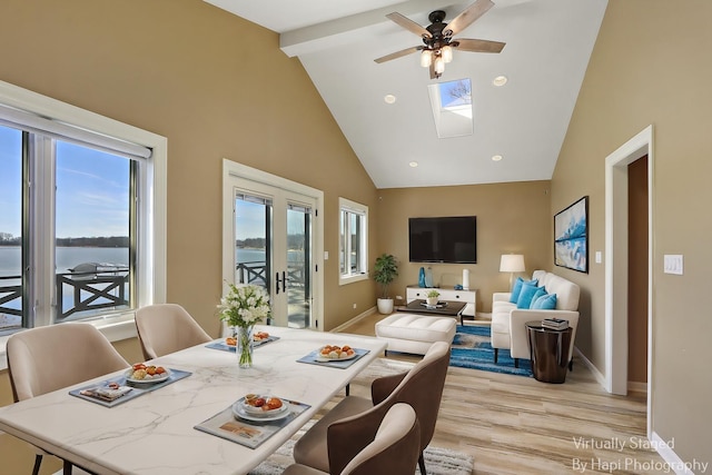 dining area with baseboards, beamed ceiling, light wood-type flooring, a skylight, and high vaulted ceiling