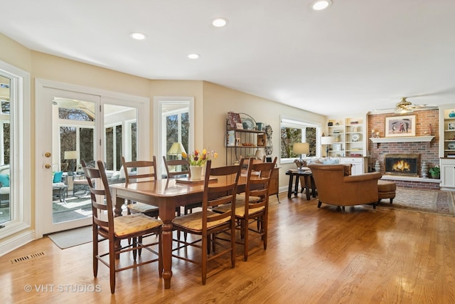 dining space with visible vents, built in shelves, wood finished floors, recessed lighting, and a brick fireplace