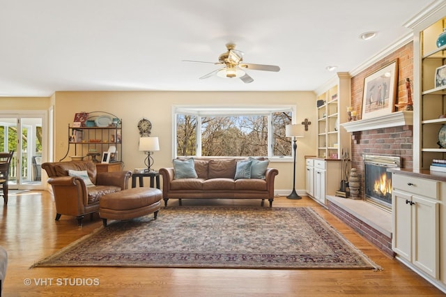 living room with a brick fireplace, light wood-type flooring, and a ceiling fan