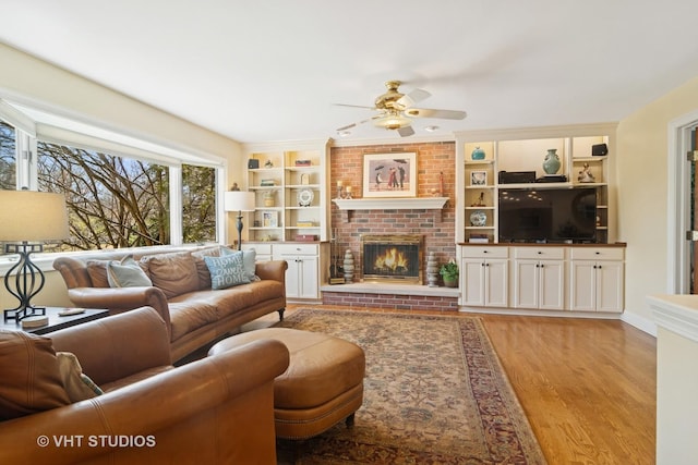 living room with a brick fireplace, built in features, light wood-type flooring, and ceiling fan