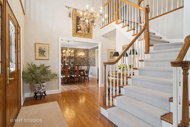 entrance foyer with baseboards, stairs, a high ceiling, an inviting chandelier, and wood finished floors