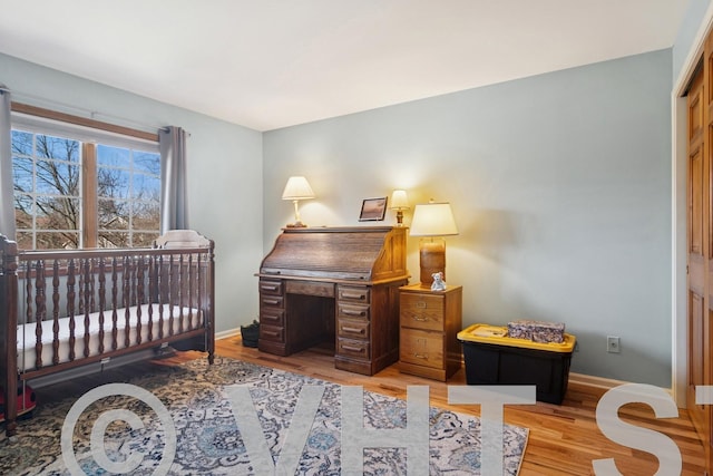 bedroom featuring light wood-style flooring, a crib, and baseboards