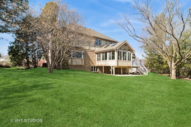 back of house with stairs, a yard, brick siding, and a sunroom