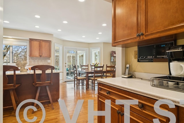 kitchen with a breakfast bar, light wood-style flooring, recessed lighting, light countertops, and brown cabinets