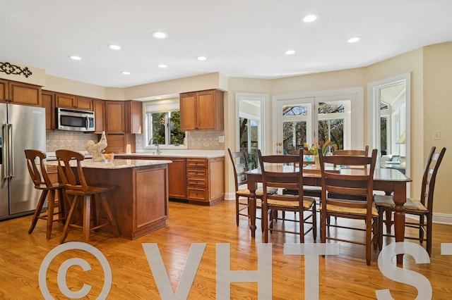 kitchen with brown cabinets, backsplash, a kitchen island, appliances with stainless steel finishes, and light wood finished floors