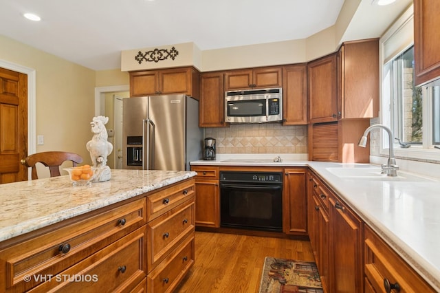 kitchen with brown cabinets, a sink, dark wood-style floors, appliances with stainless steel finishes, and decorative backsplash