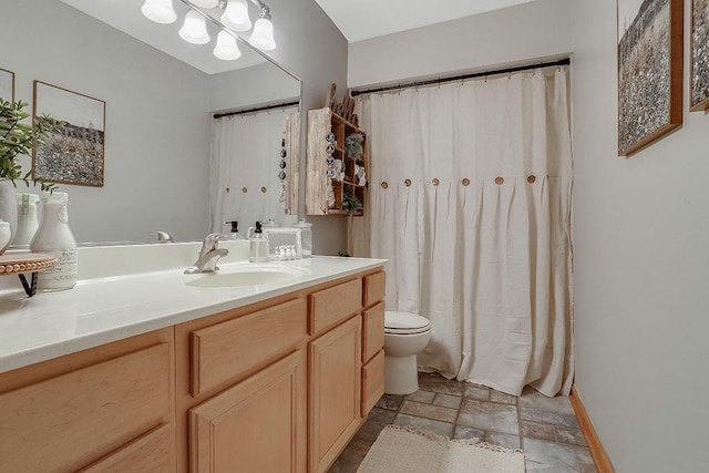 bathroom featuring toilet, baseboards, stone tile flooring, and vanity