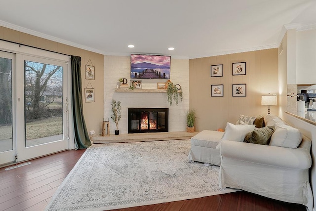 living room with a brick fireplace, wood finished floors, visible vents, and crown molding