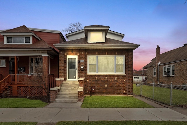 view of front of property featuring a yard, brick siding, a porch, and fence