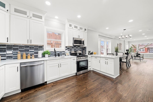 kitchen featuring a peninsula, appliances with stainless steel finishes, light countertops, and dark wood-type flooring