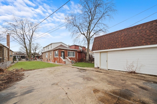 view of property exterior featuring an outbuilding, fence, a yard, driveway, and roof with shingles