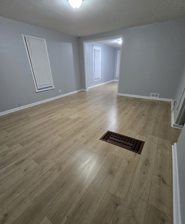 empty room featuring light wood-style floors, baseboards, and visible vents