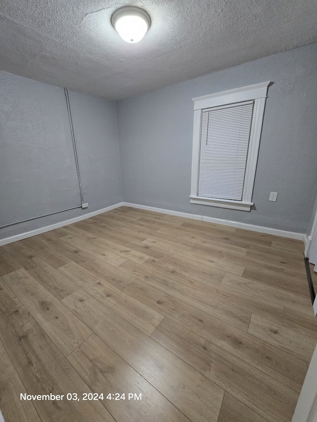 unfurnished room with a textured ceiling, baseboards, and wood finished floors