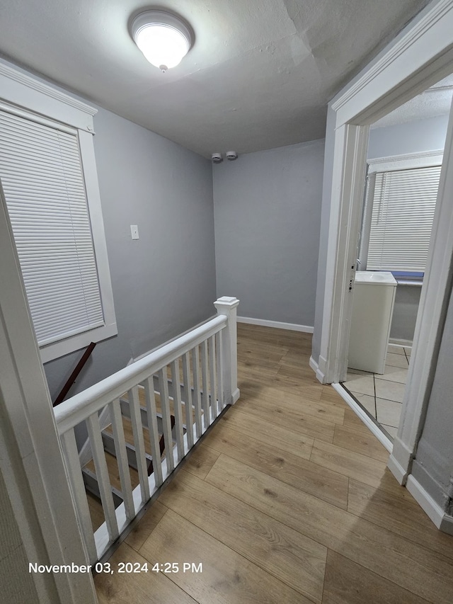 corridor with baseboards, an upstairs landing, and wood finished floors