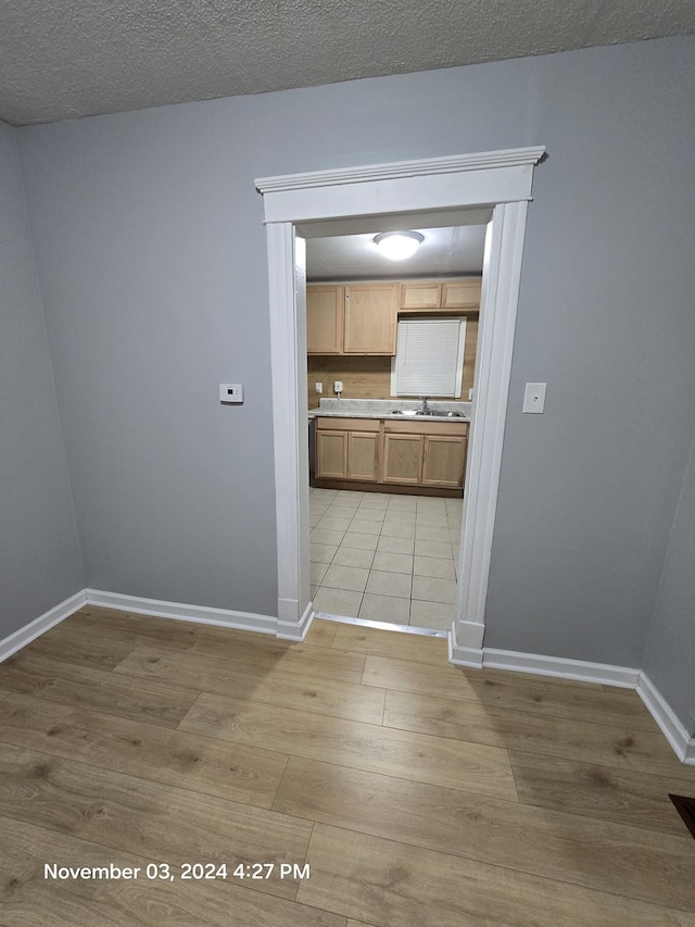 interior space featuring baseboards, a sink, a textured ceiling, and light wood finished floors