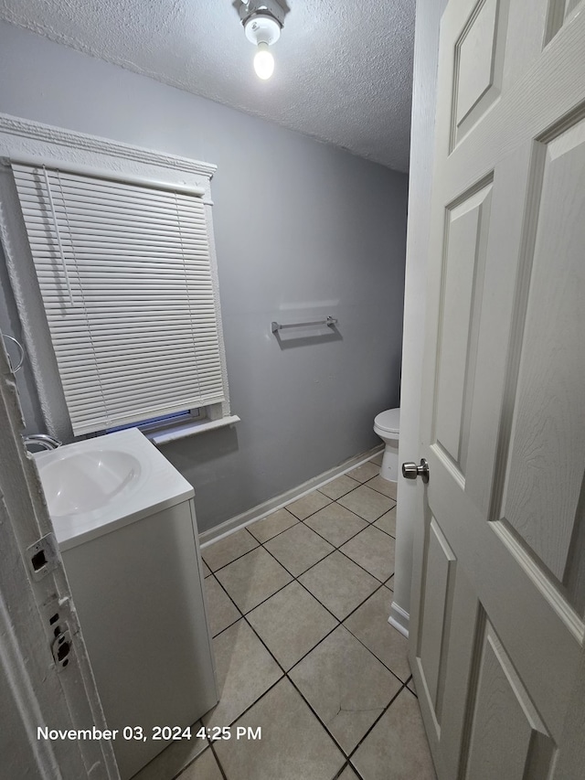 half bath with baseboards, toilet, tile patterned floors, a textured ceiling, and vanity