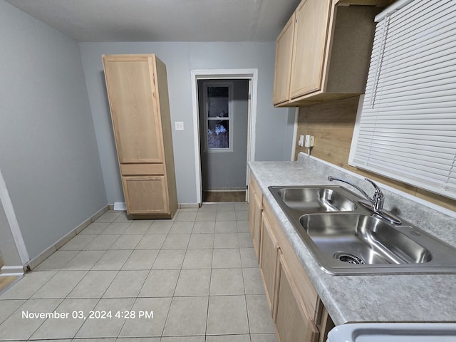 kitchen with light tile patterned floors, a sink, baseboards, light countertops, and light brown cabinetry