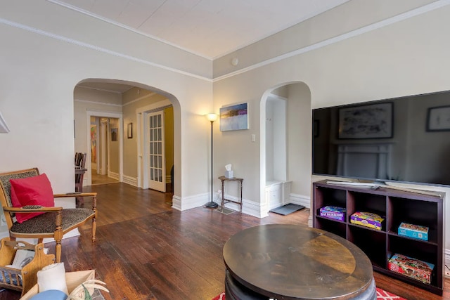 living area featuring arched walkways, baseboards, wood finished floors, and crown molding