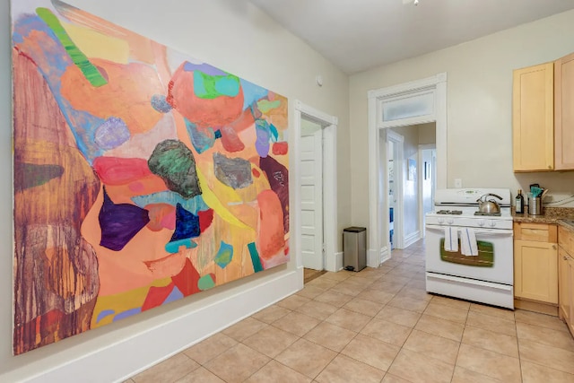 kitchen featuring light tile patterned floors, white gas range, and light brown cabinetry