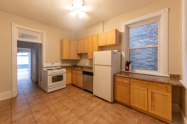 kitchen featuring light tile patterned flooring, white appliances, a sink, dark stone counters, and light brown cabinetry