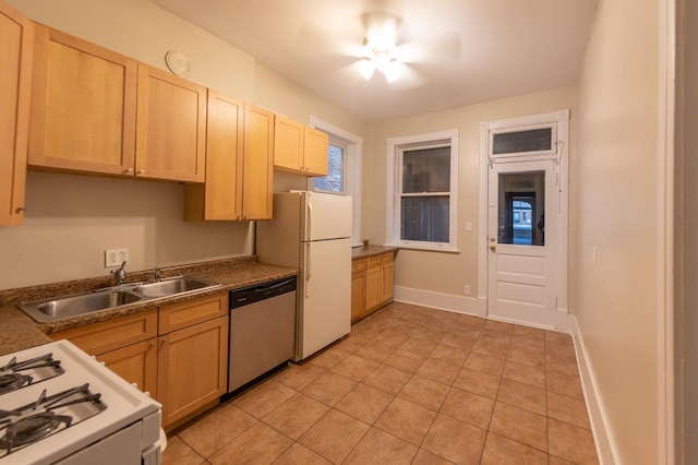 kitchen with light tile patterned floors, light brown cabinetry, a sink, white appliances, and baseboards