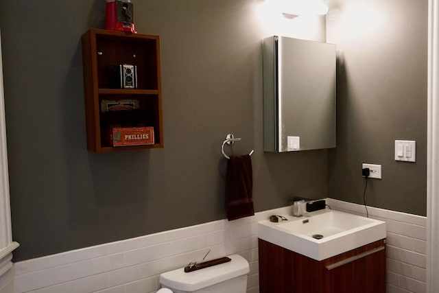 bathroom featuring toilet, vanity, tile walls, and wainscoting